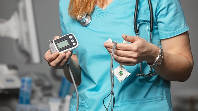 A close-up image of a woman holding ECG holter monitor 
