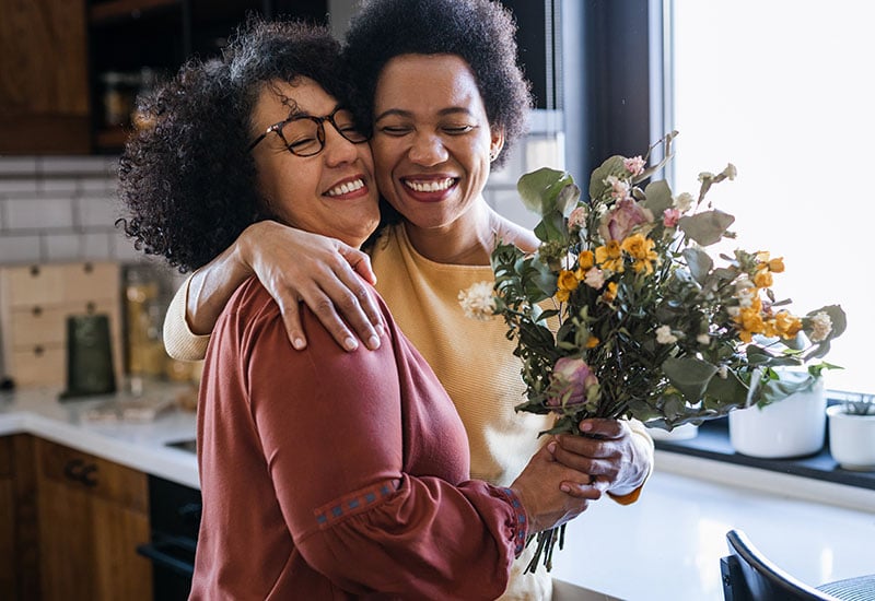 two women standing in a kitchen holding flowers