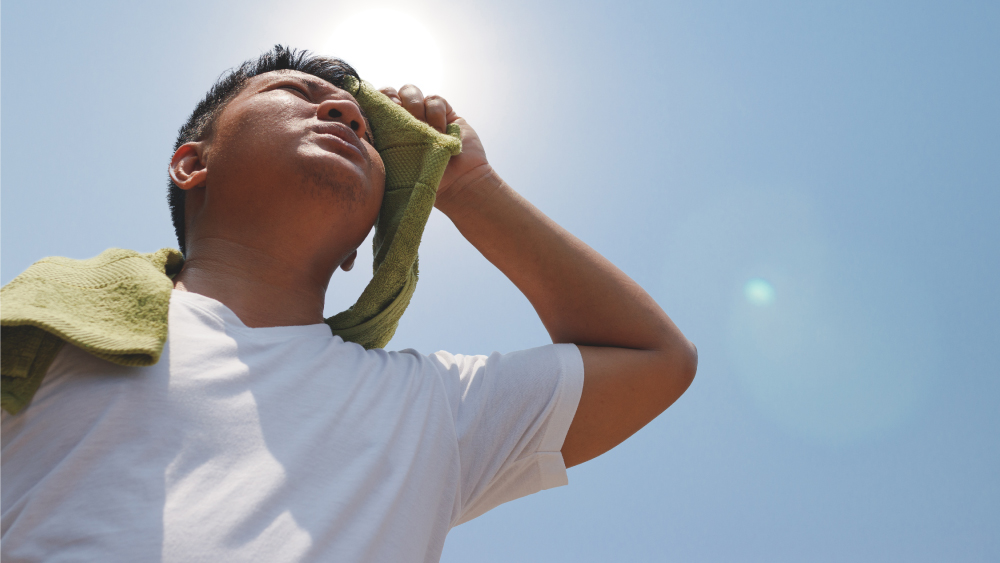 man in white t-shirt wipes sweat with green towel as sun beats down overhead