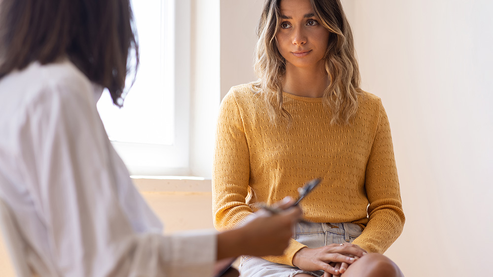 Female patient in yellow sweater denim skirt talking with female healthcare provider