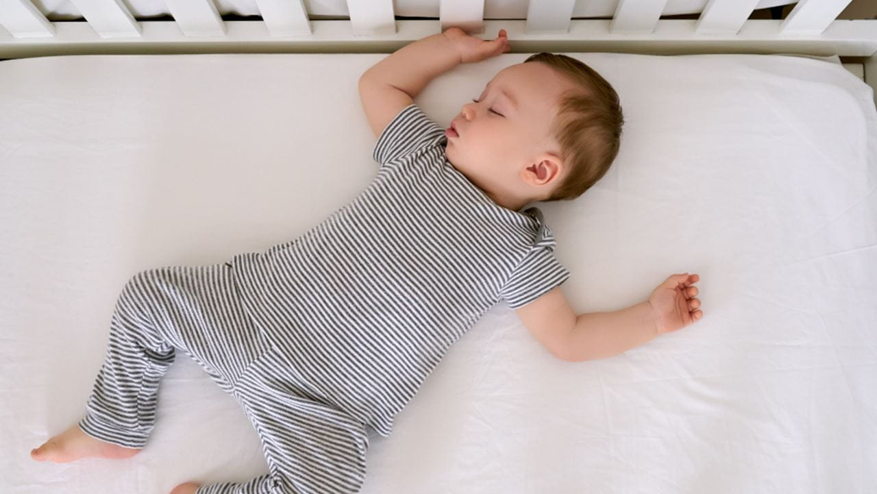 White infant asleep on his back in a crib