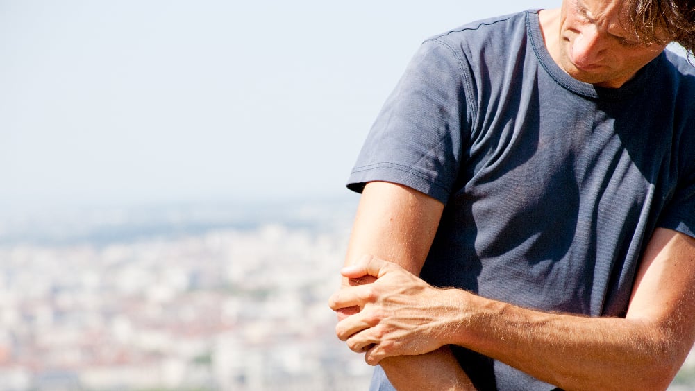 Middle aged white man in blue shirt holds elbow