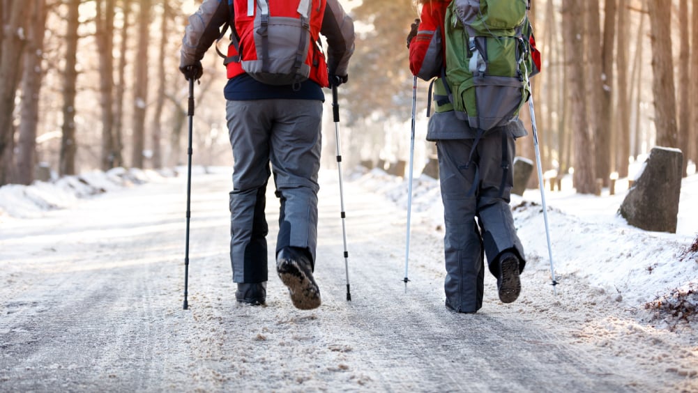 Two people hiking on snowy trail with walking poles