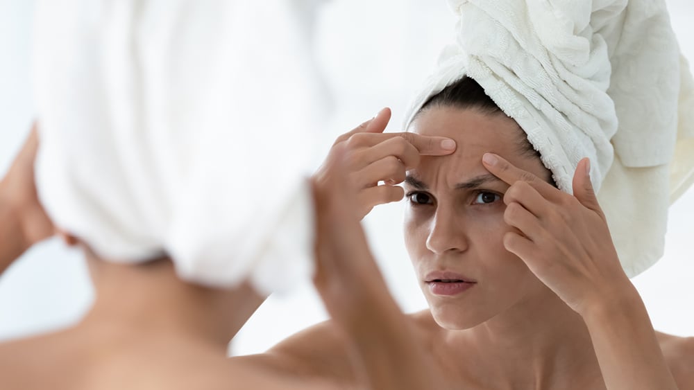Woman looking at acne on forehead
