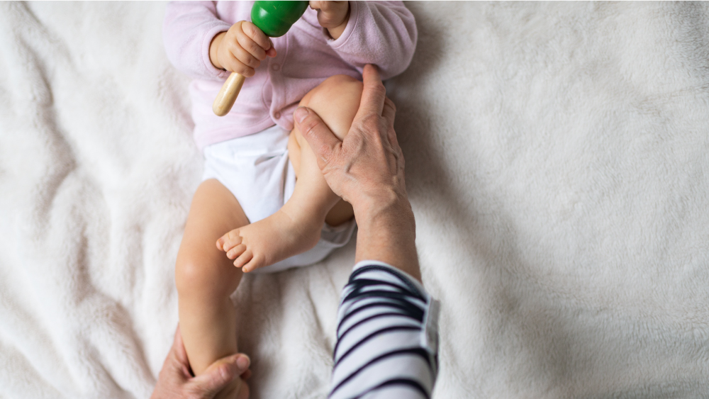 infant in pink long sleeve shirt and cloth diaper having legs moved by adult