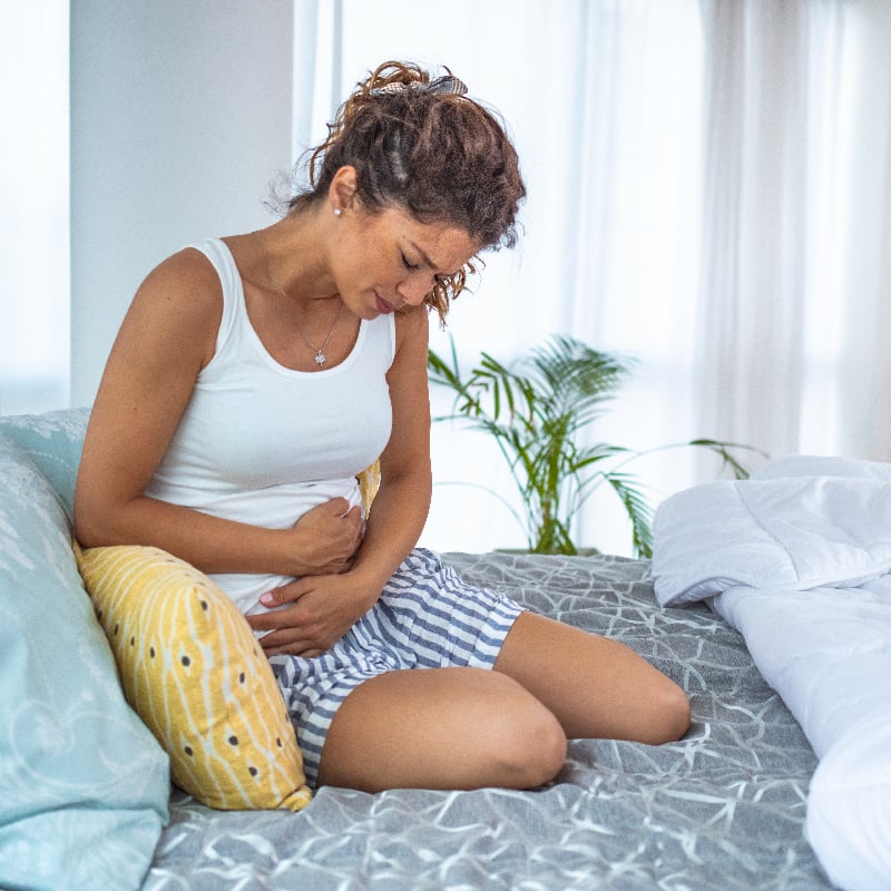 female sitting down holding her stomach in pain