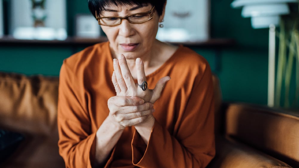 elderly female sitting down holding her hand in pain