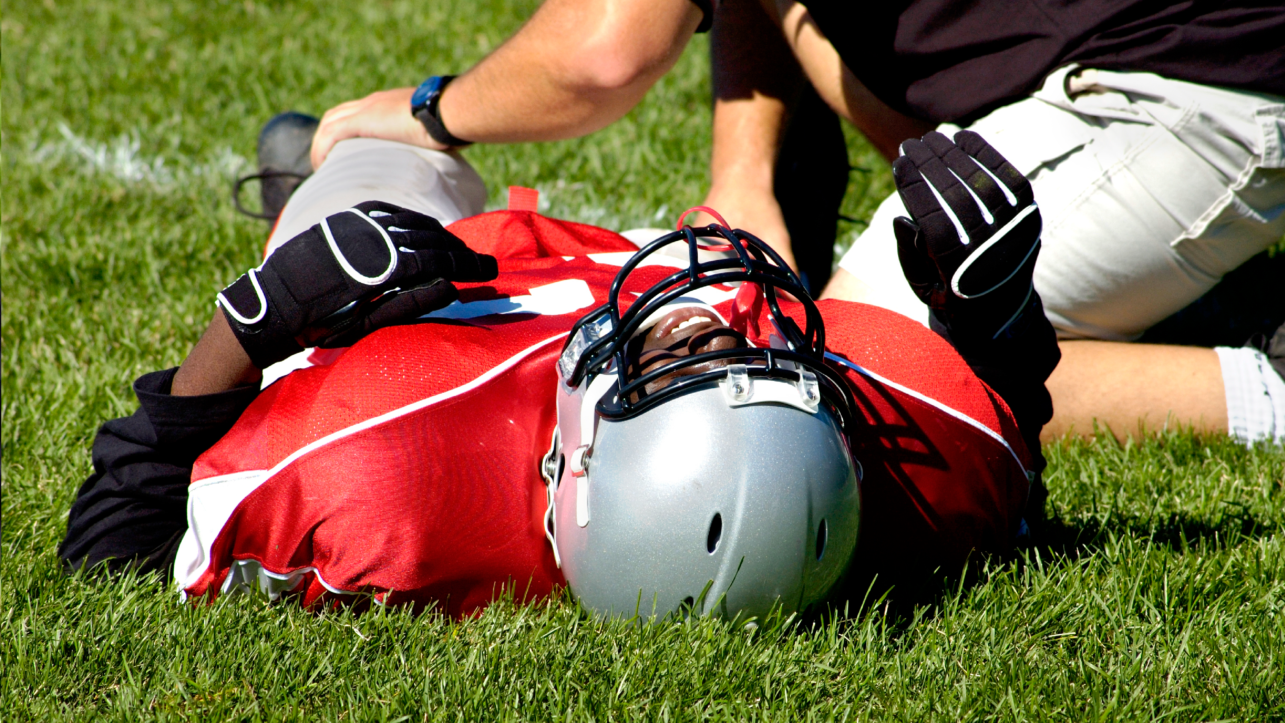 football player laying on field being checked by athletic trainer