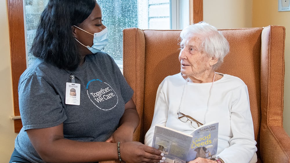 Black nurse with mask reading to elderly white patient