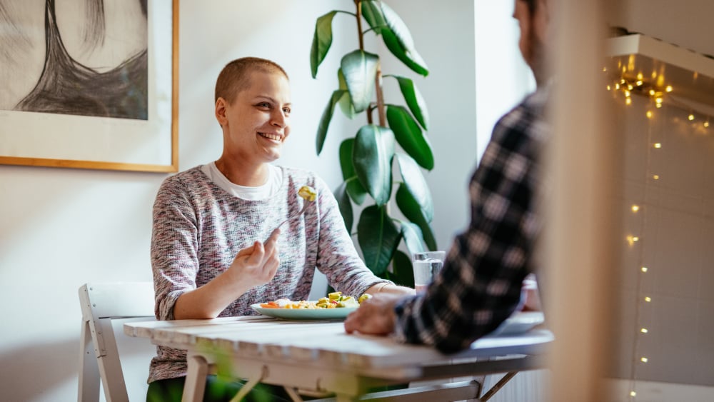 A woman with a shaved head eats off of a plate while smiling