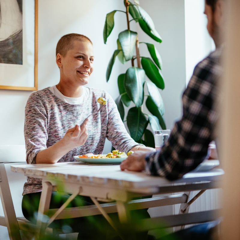A woman with a shaved head eats off of a plate while smiling