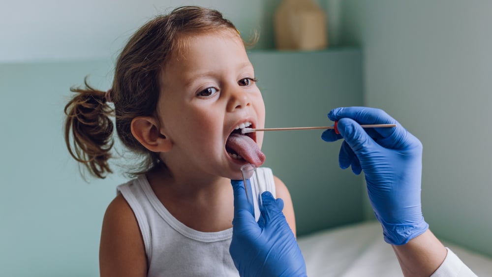 A young White girl gets a throat swab from a physician