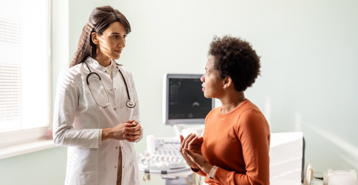 A White female doctor talks with a Black female patient in an office setting