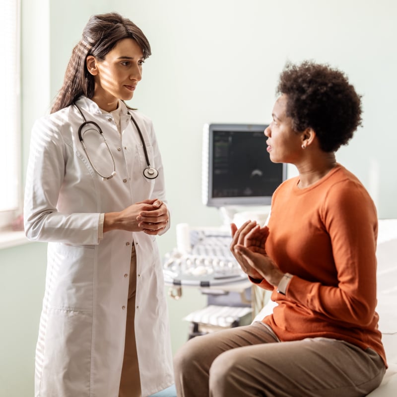 A White female doctor talks with a Black female patient in an office setting