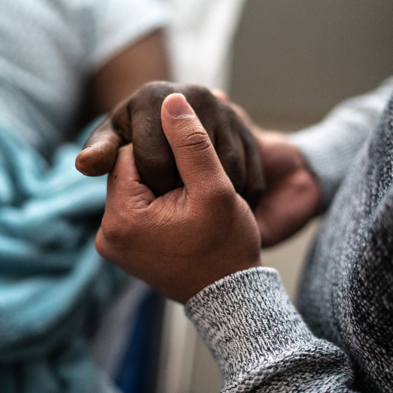 A family member holds the hand of a hospice patient