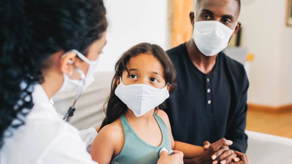 A young girl and her father sit with a provider - all wearing face masks