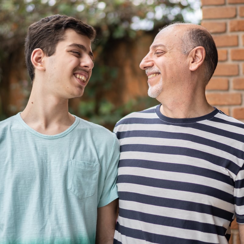 A white teenage boy and a white middle-aged man smile at one another