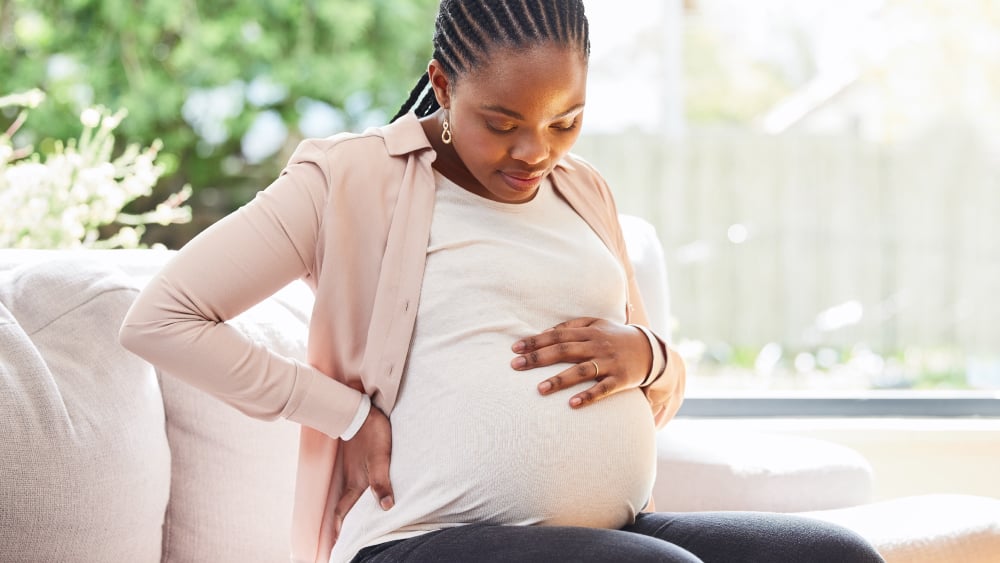 A pregnant Black woman sits on a couch