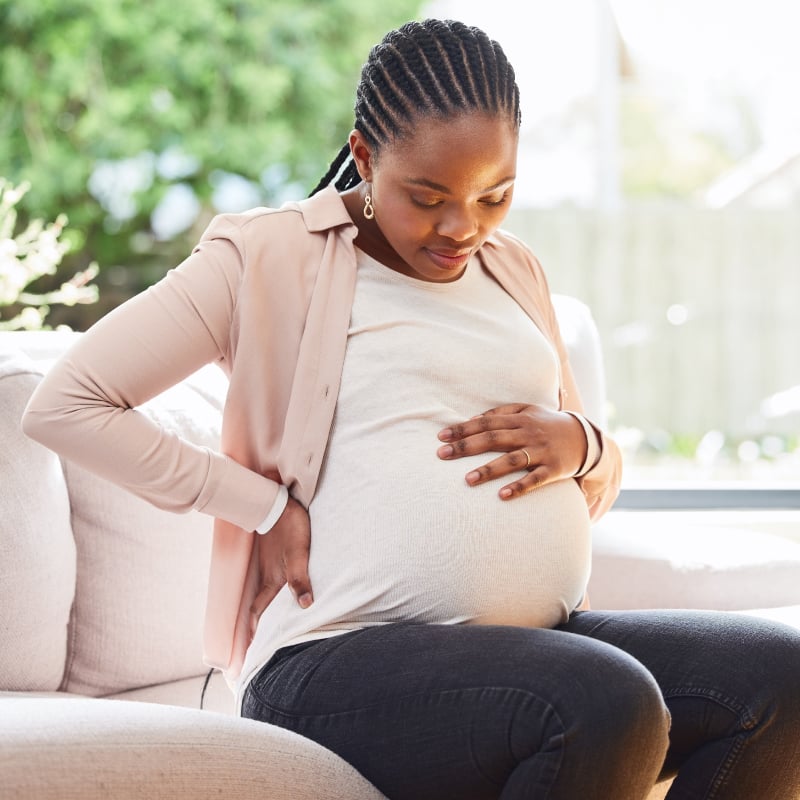 A pregnant Black woman sits on a couch