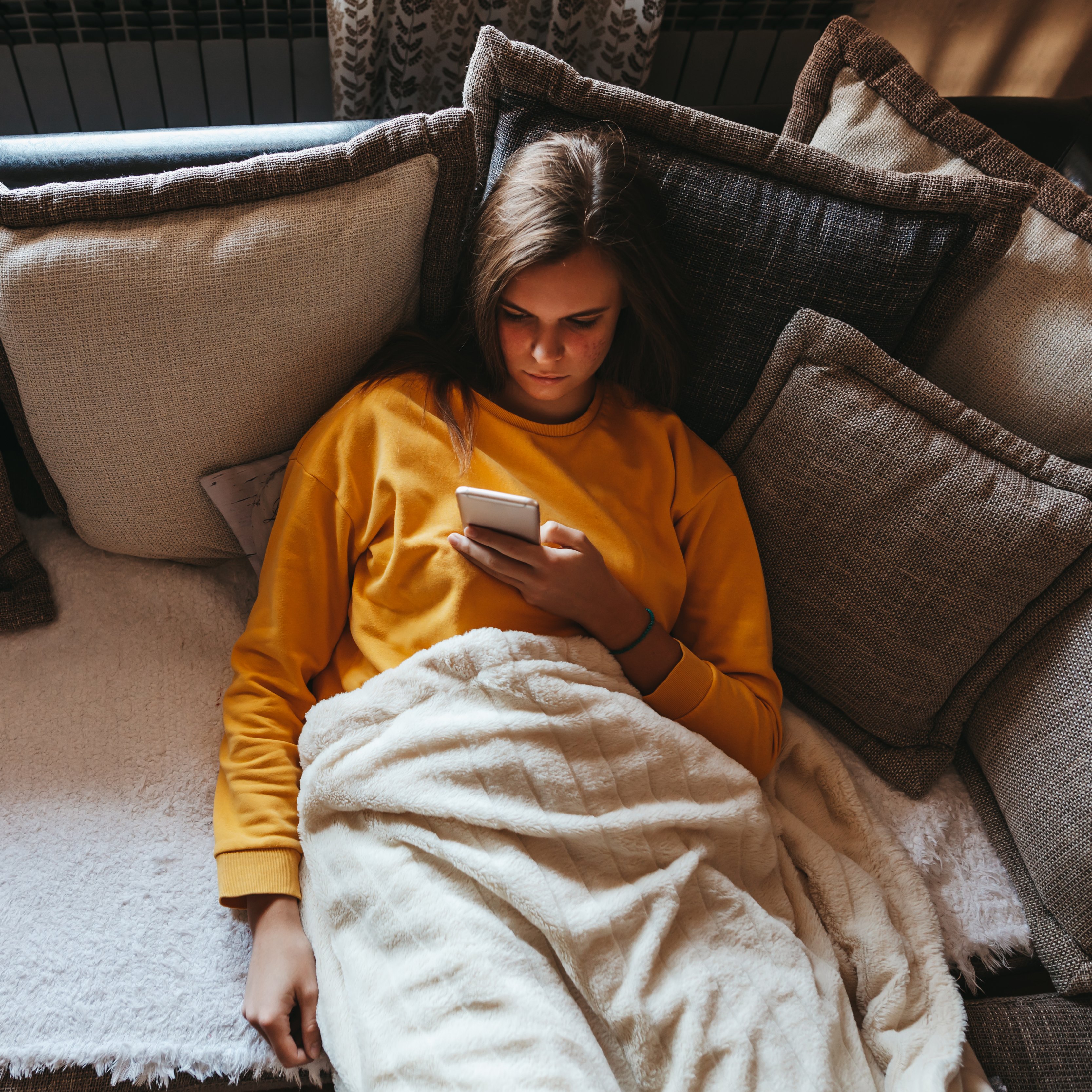 A young woman on a couch scrolling on her smartphone