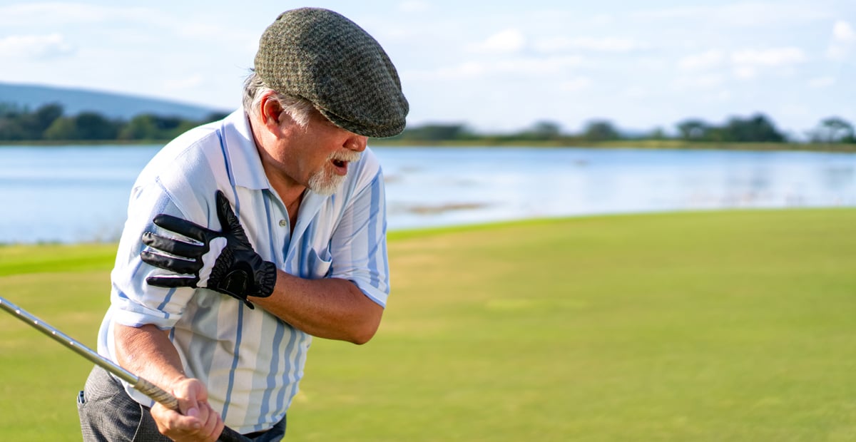 An older white male golfer grabs his shoulder in pain