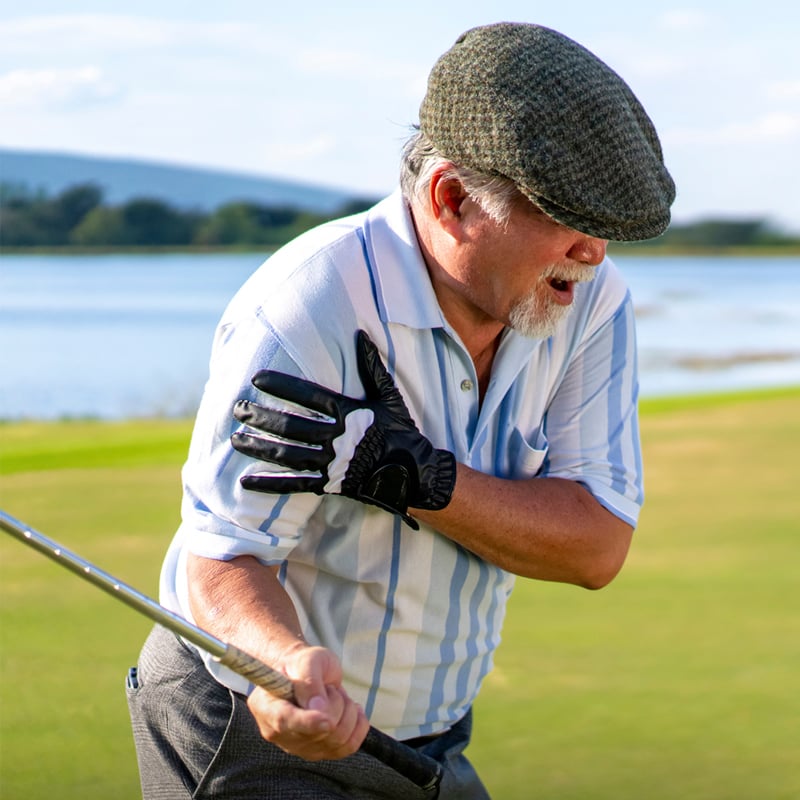 An older white male golfer grabs his shoulder in pain