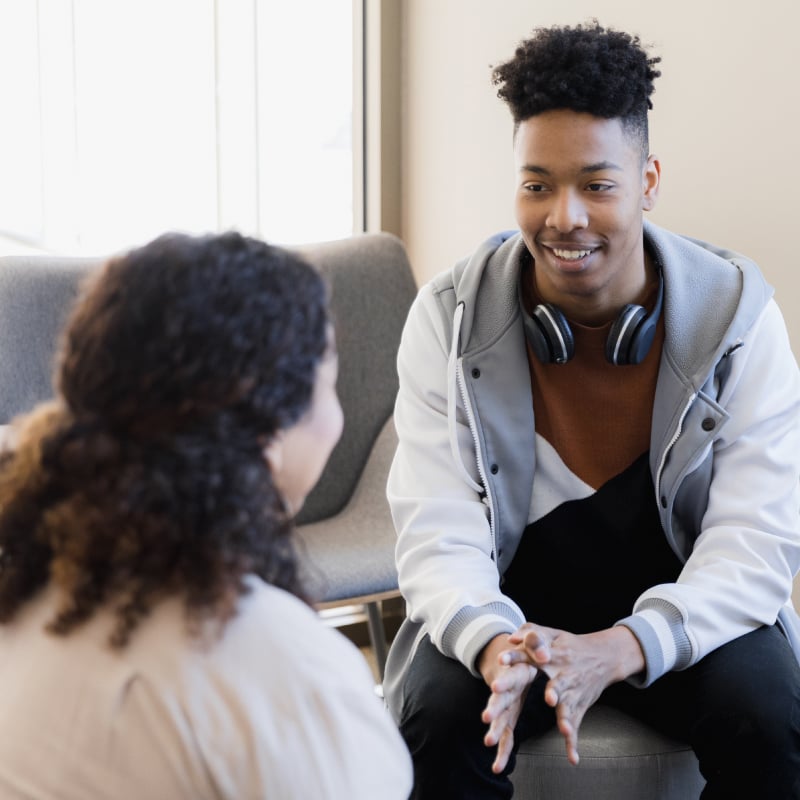 A young Black male teenager talks with a Black female therapist