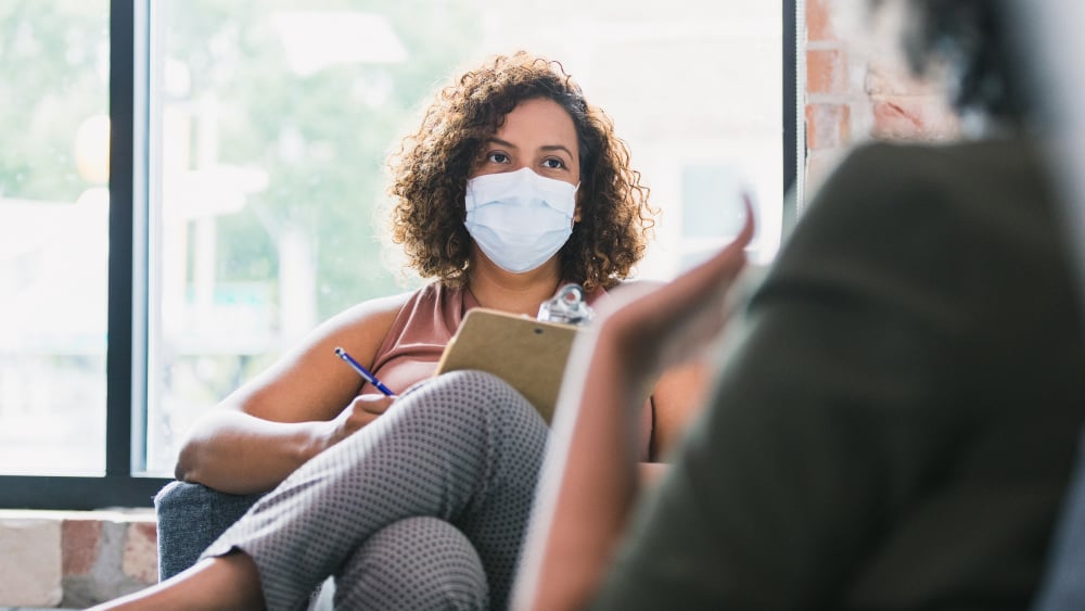 A woman wearing a mask talks with a therapist