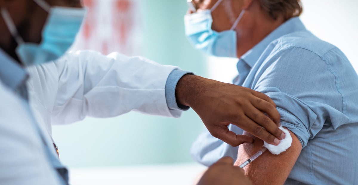 A patient wearing a mask is given an injection by a medical provider