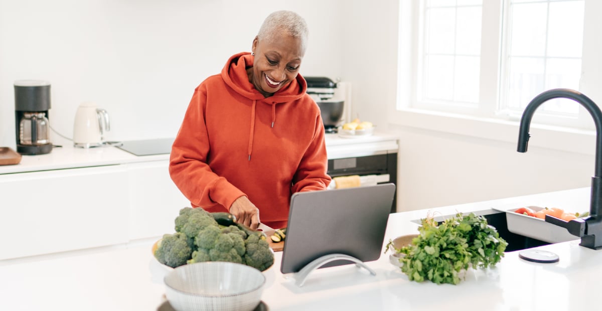 A middle-aged Black woman chops vegetables in the kitchen