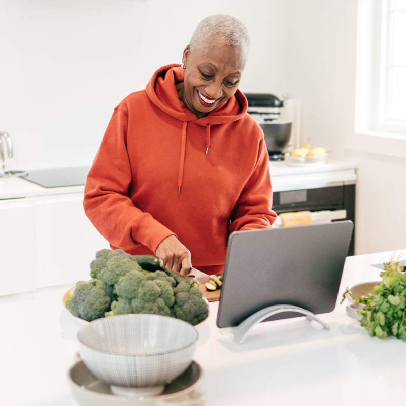 A middle-aged Black woman chops vegetables in the kitchen