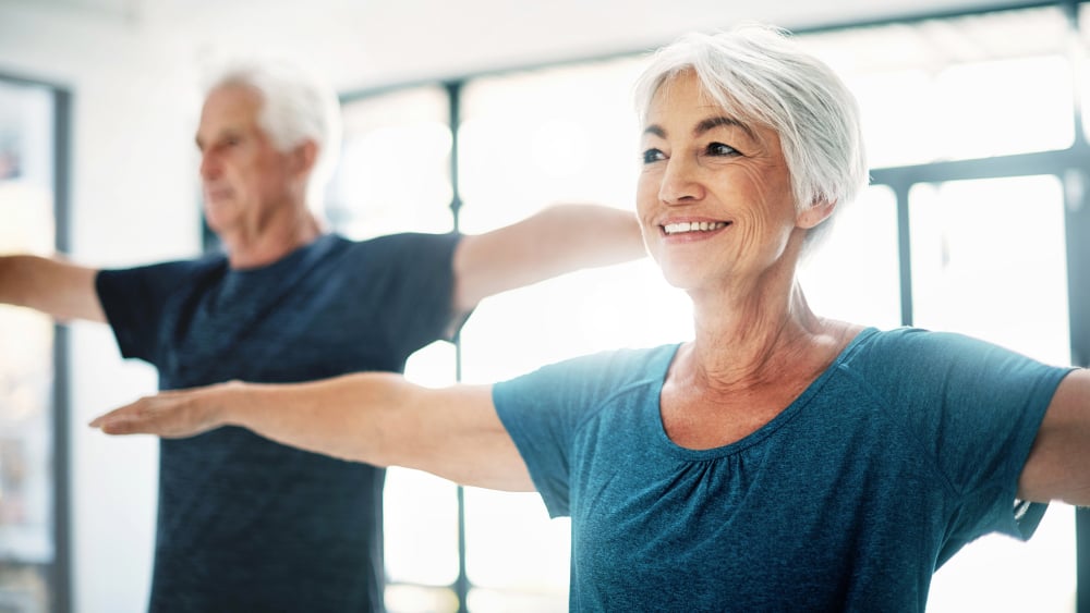 An older White man and older White woman stretch their arms while smiling