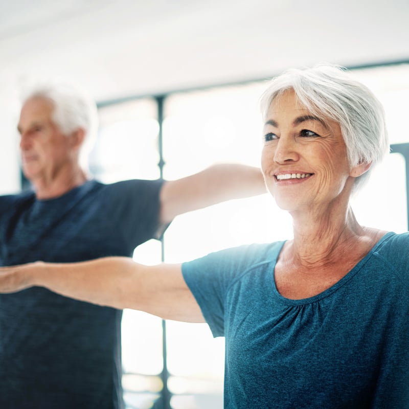 An older White man and older White woman stretch their arms while smiling