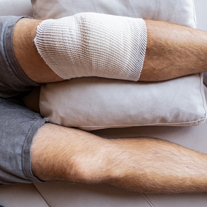 A person with their knee wrapped in a bandage and sitting on a pillow