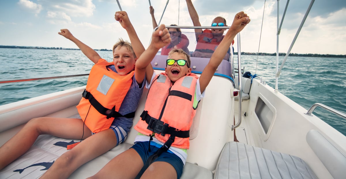 Two children and two adults wearing life jackets are excited riding on a boat
