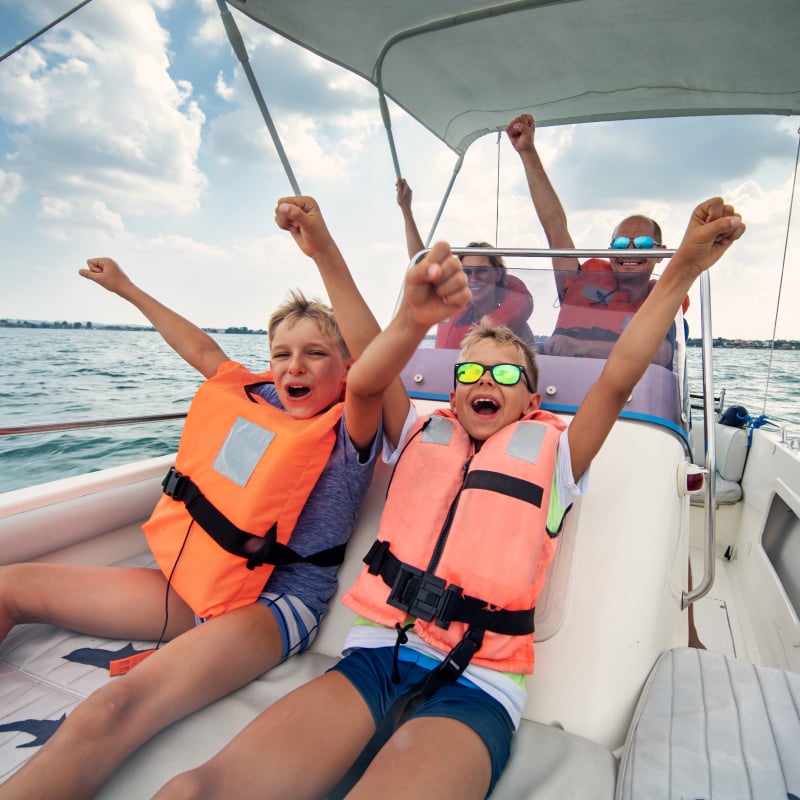 Two children and two adults wearing life jackets are excited riding on a boat