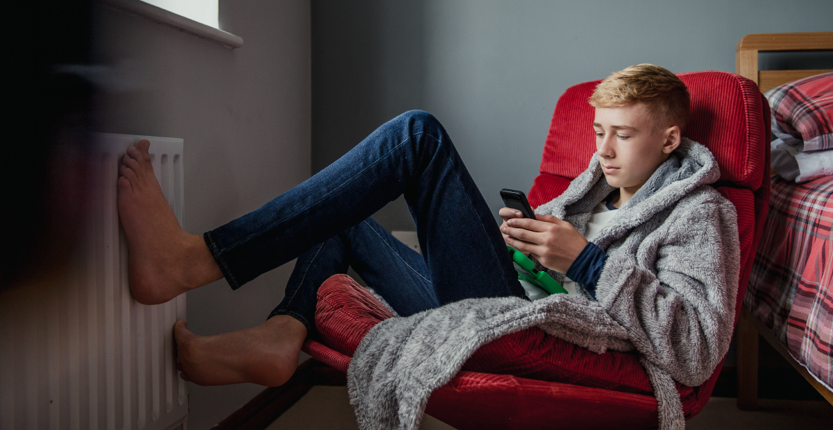 A White teenage boy sits in a red chair and looks at a smartphone