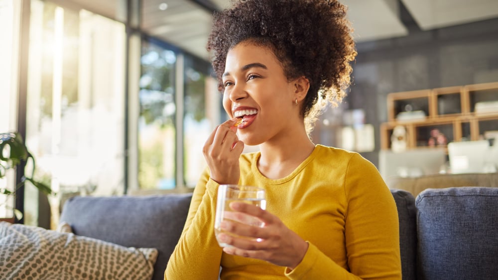 A smiling woman takes an oral supplement