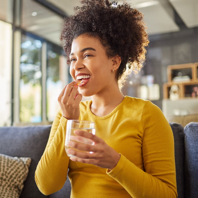 A smiling woman takes an oral supplement