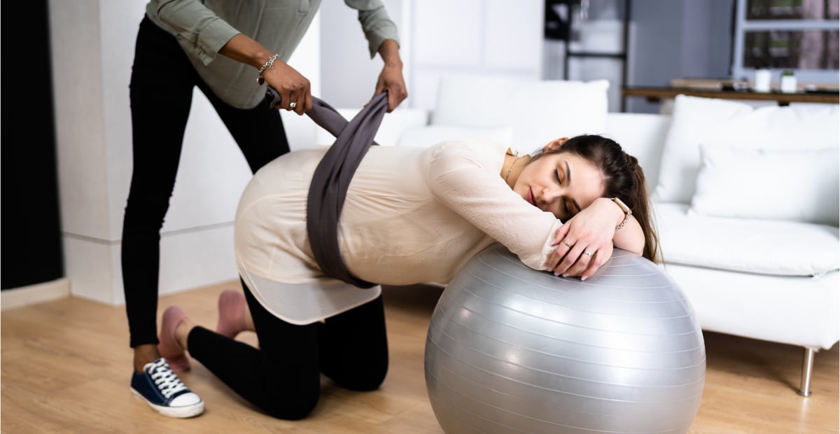 A doula helps a pregnant person near an exercise ball
