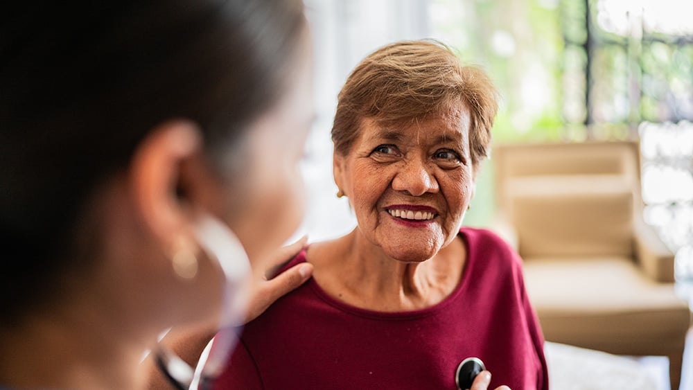 Home caregiver listening to a senior woman's heartbeat in a nursing home