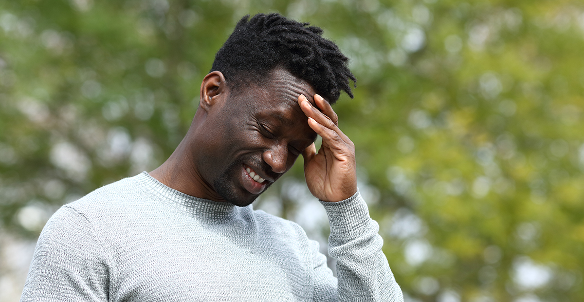 Black man suffering from painful head ache touching his temple with hand in a park