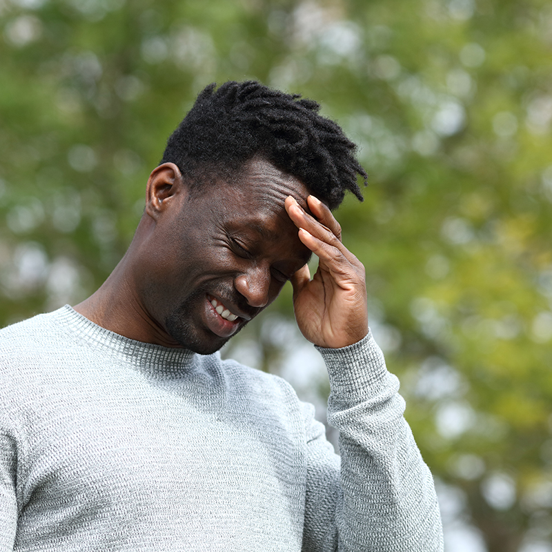 Black man suffering from painful head ache touching his temple with hand in a park