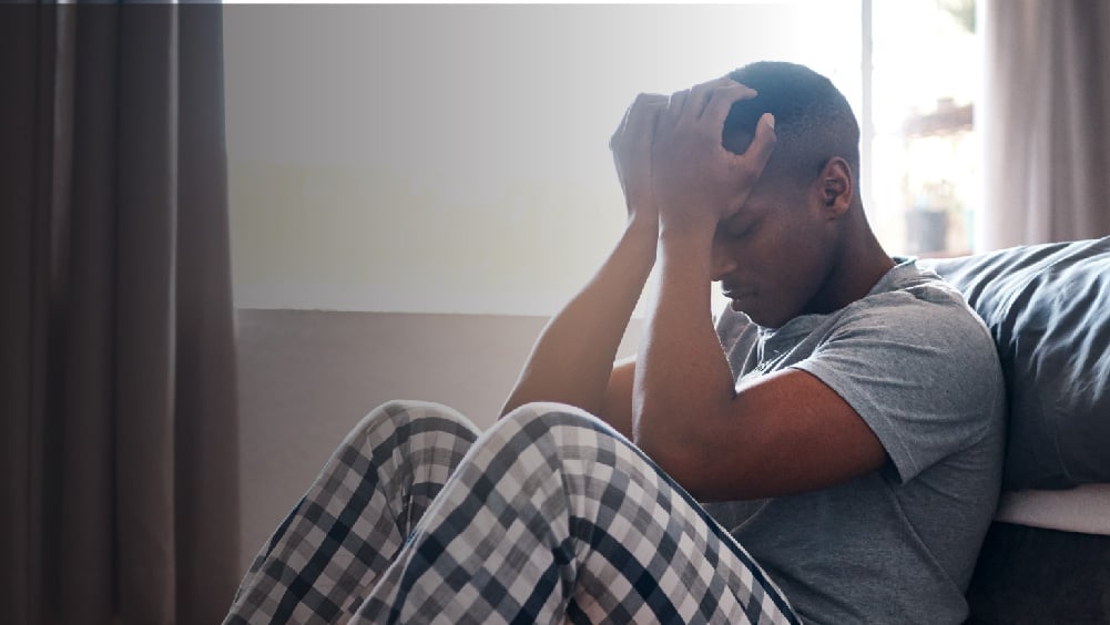 Man sitting down next to bed with head in hands
