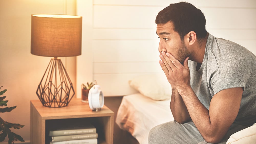 Man sitting on bed with hands cupped over mouth