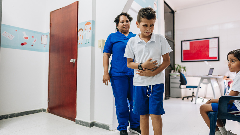 Child holding stomach in pain with nurse behind him