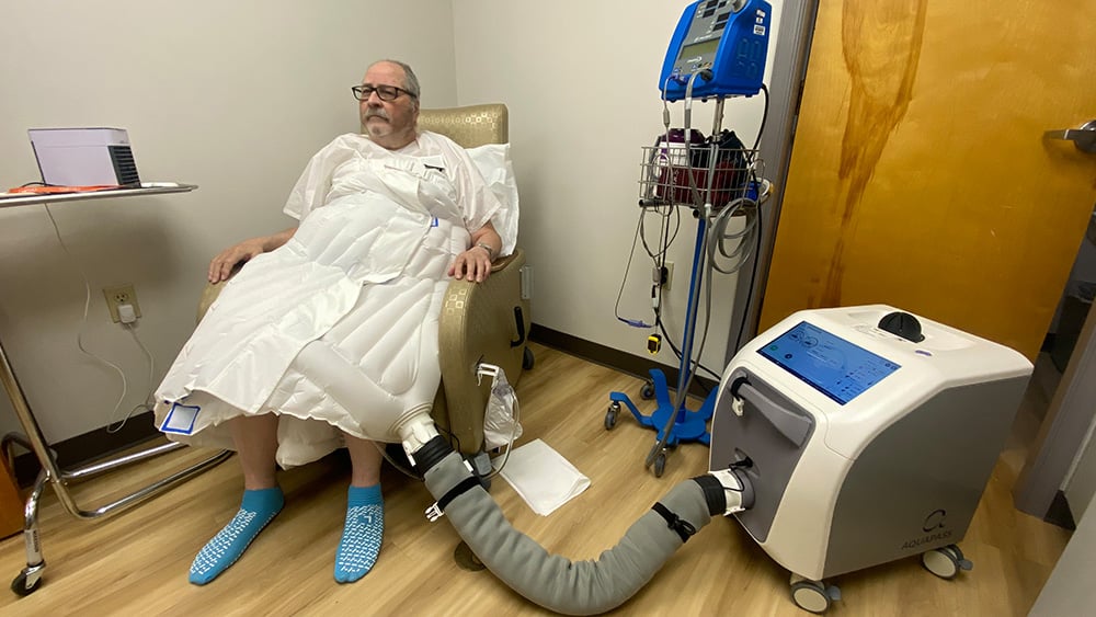 Man in special medical suit sits in hospital chair for therapy