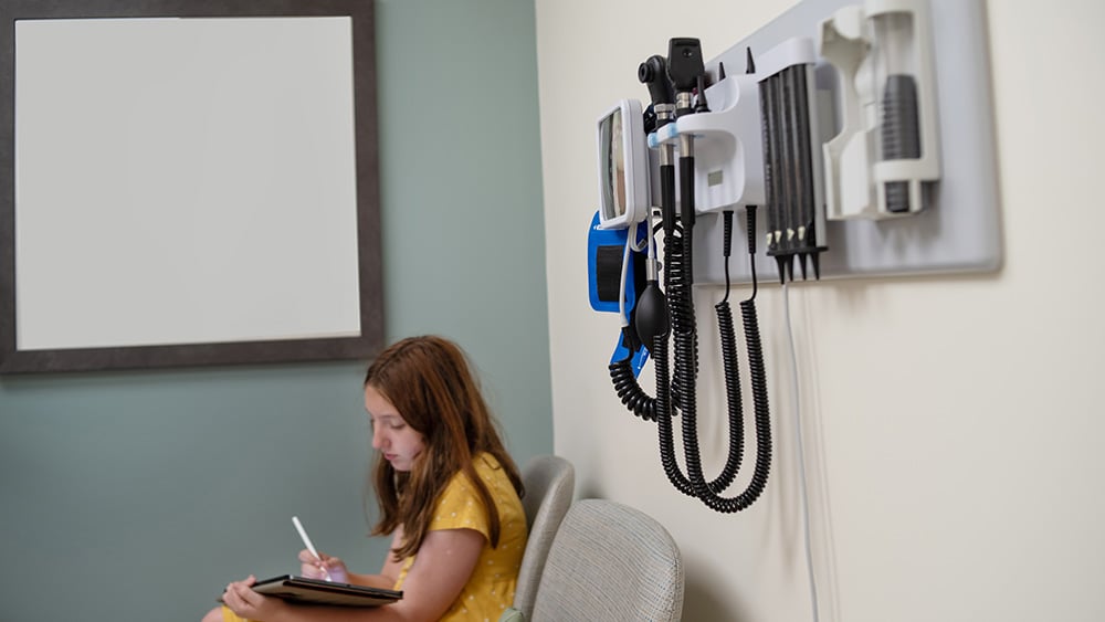 Young girl in yellow dress sits in doctor's examination room while waiting for her annual back-to-school check-up