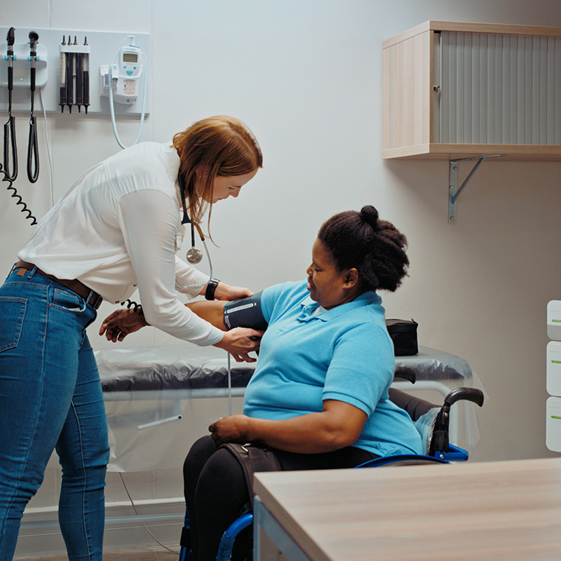 Woman doctor taking patient blood pressure in hospital consultation or examination room