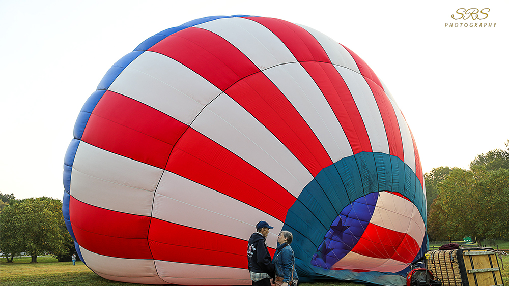 Man and woman face one another talking in front of red white and blue hot air balloon